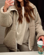 Studio shot of a women's oversized, cream/off-white teddy bear fleece (borg) jacket. The jacket features a high stand-up funnel collar, a full silver zip closure, two large front patch pockets, and subtle contrast seam detailing on the arms and body. The silhouette is boxy and warm.