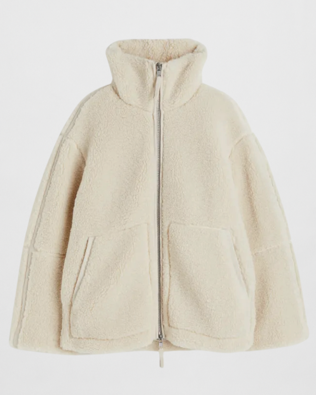 Studio shot of a women's oversized, cream/off-white teddy bear fleece (borg) jacket. The jacket features a high stand-up funnel collar, a full silver zip closure, two large front patch pockets, and subtle contrast seam detailing on the arms and body. The silhouette is boxy and warm.