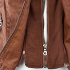 Studio shot of a women's fitted faux leather biker jacket in a warm cognac/light brown colour. The jacket has a front zipper closure, zippered chest and side pockets, detailed quilted shoulder and cuff panels, and an integrated fabric hood with drawstrings. The fit is clearly tailored and slim. Focus on the fitted silhouette and the texture of the faux leather.