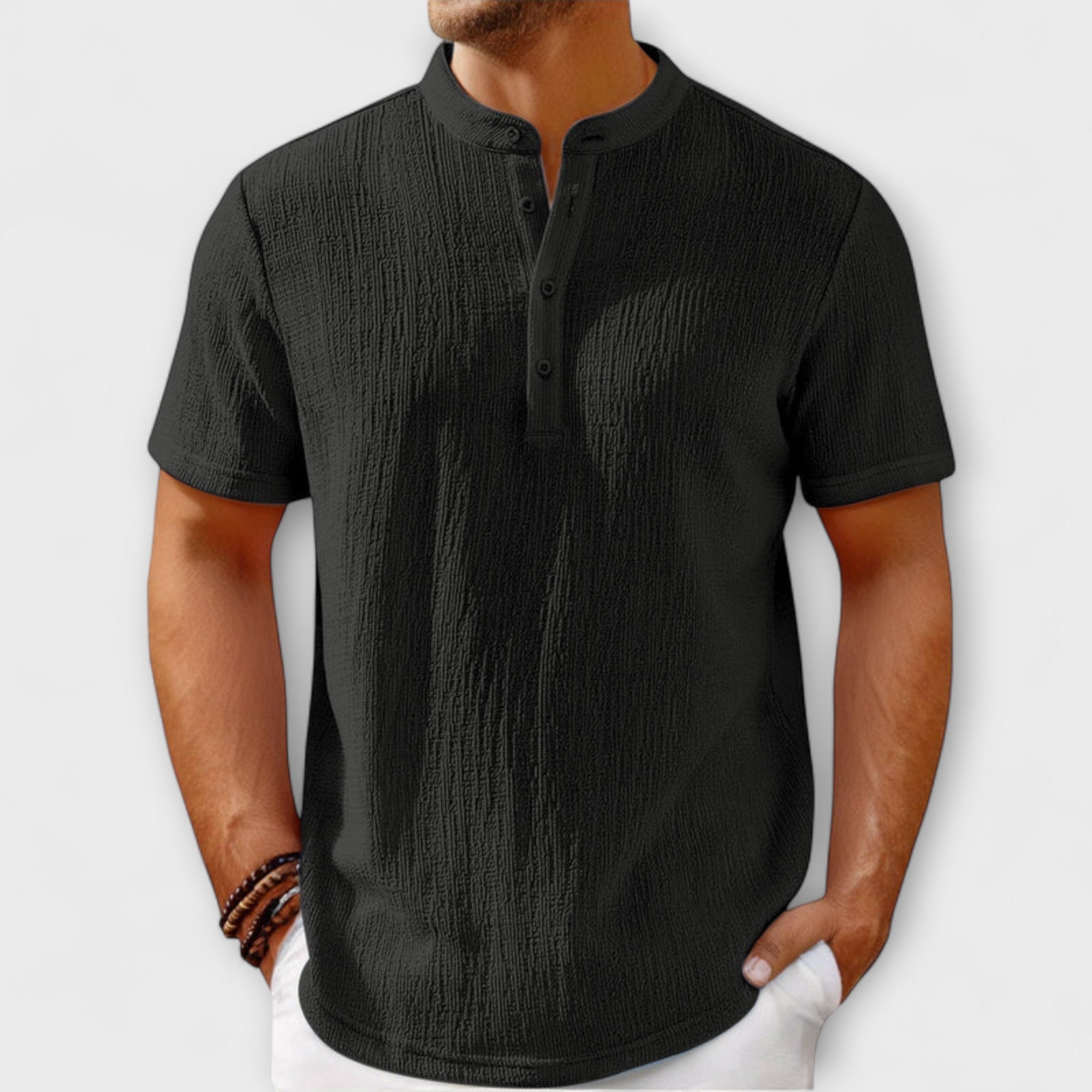 Men's short-sleeve, band-collar Henley shirt in a light cream/off-white textured linen blend fabric. The shirt has a three-button placket. The model is standing with hands in white trousers pockets, showing the relaxed fit. Focus on the linen-blend texture and the minimalist collar design.