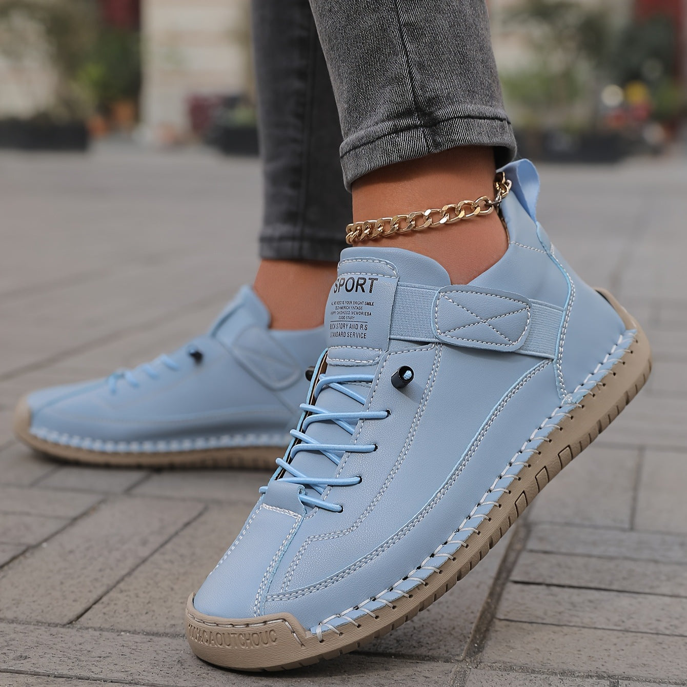 A close-up of the ALTHORA Urban Stitch Walker, a white leather casual sneaker with prominent tan moccasin-style stitching around the edges and a matching tan rubber outsole. The shoe has white laces and a small 'SPORT' label on the tongue.