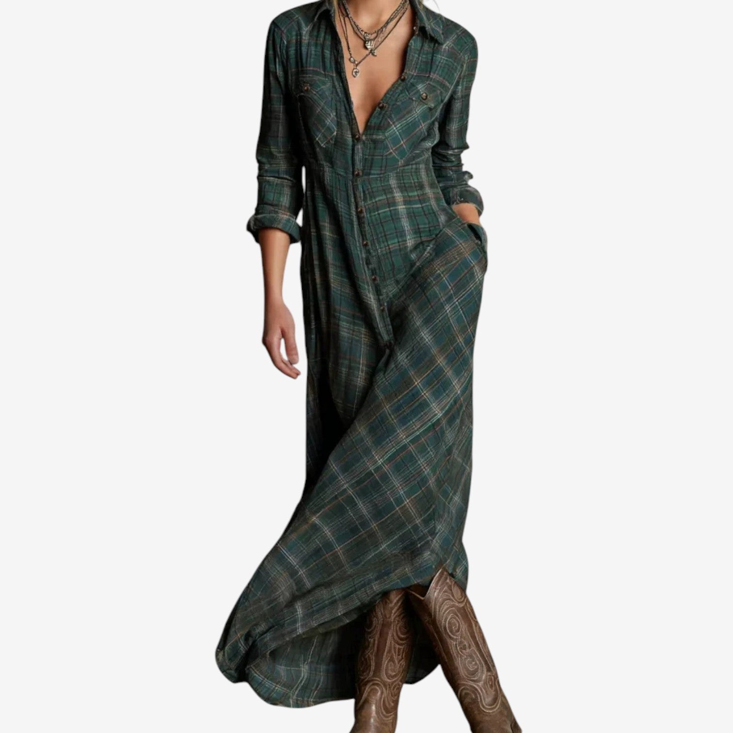 Full-length image of a woman modelling a maxi-length shirt dress in a rustic green, brown, and cream plaid/check pattern. The dress features a button-up front, a collar, and long sleeves that are rolled up. A matching fabric belt is tied around the waist, and the skirt flows to the ankles. Focus on the fabric pattern, the dress's length, and the waist-cinching detail.