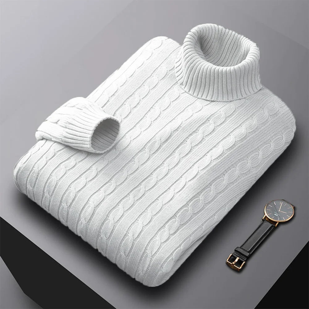 Folded men's turtleneck/roll-neck jumper in a light beige/oatmeal colour. The knit features a subtle vertical cable pattern down the body. The turtleneck and cuffs are ribbed. The sweater is styled next to a black leather men's wristwatch. Focus on the fine cable texture and the clean fold.