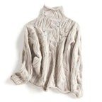 Overhead view of a folded light beige/cream women's high neck/turtleneck jumper. The knit features an elaborate, open-work lace and cable pattern. The garment has a soft, thick appearance and the funnel neck is clearly visible. Focus on the intricate, highly textured stitch work.