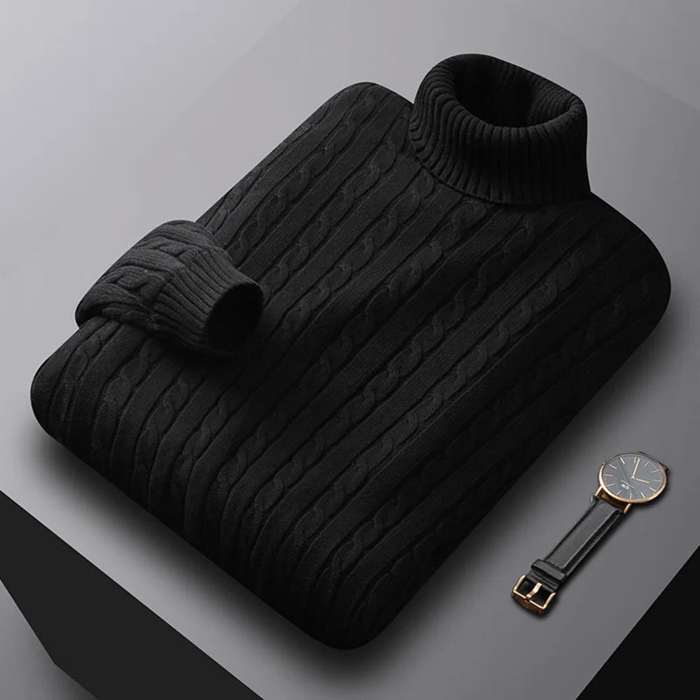 Folded men's turtleneck/roll-neck jumper in a light beige/oatmeal colour. The knit features a subtle vertical cable pattern down the body. The turtleneck and cuffs are ribbed. The sweater is styled next to a black leather men's wristwatch. Focus on the fine cable texture and the clean fold.