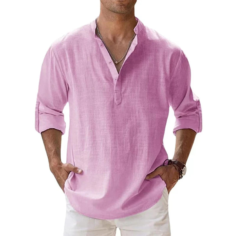 Men's long-sleeve popover shirt in white, featuring a Grandad/band collar and a short buttoned Henley placket. The shirt is made from a light, textured linen-blend fabric. The model is standing with hands in pockets, showcasing the relaxed, slightly oversized fit and rolled-up sleeves. Focus on the texture and the minimalist collar.