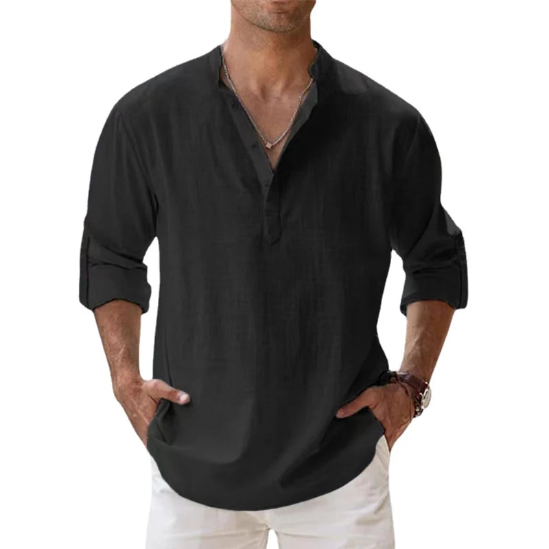 Men's long-sleeve popover shirt in white, featuring a Grandad/band collar and a short buttoned Henley placket. The shirt is made from a light, textured linen-blend fabric. The model is standing with hands in pockets, showcasing the relaxed, slightly oversized fit and rolled-up sleeves. Focus on the texture and the minimalist collar.