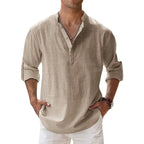 Men's long-sleeve popover shirt in white, featuring a Grandad/band collar and a short buttoned Henley placket. The shirt is made from a light, textured linen-blend fabric. The model is standing with hands in pockets, showcasing the relaxed, slightly oversized fit and rolled-up sleeves. Focus on the texture and the minimalist collar.