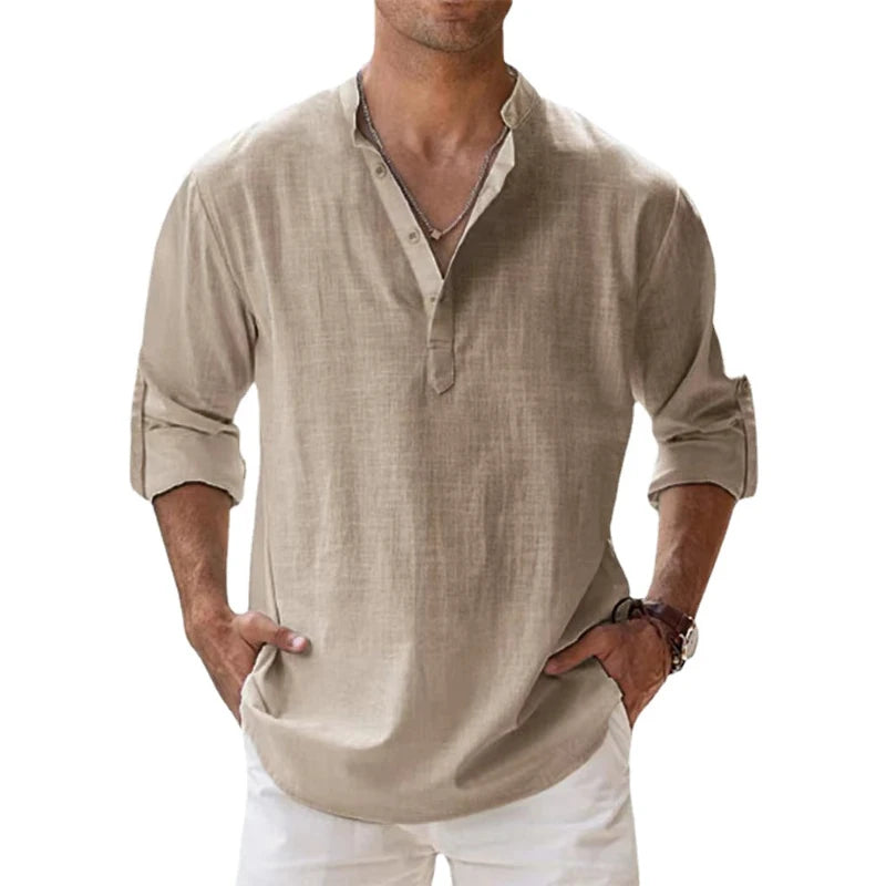Men's long-sleeve popover shirt in white, featuring a Grandad/band collar and a short buttoned Henley placket. The shirt is made from a light, textured linen-blend fabric. The model is standing with hands in pockets, showcasing the relaxed, slightly oversized fit and rolled-up sleeves. Focus on the texture and the minimalist collar.