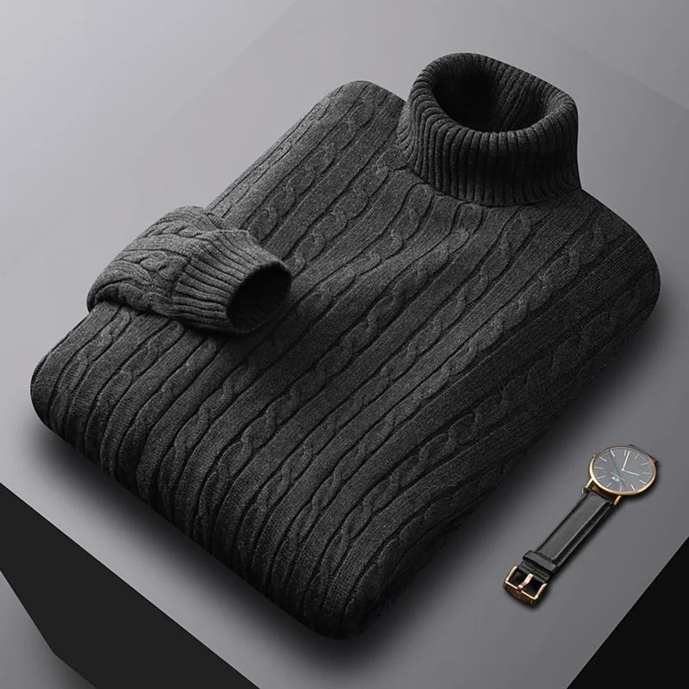 Folded men's turtleneck/roll-neck jumper in a light beige/oatmeal colour. The knit features a subtle vertical cable pattern down the body. The turtleneck and cuffs are ribbed. The sweater is styled next to a black leather men's wristwatch. Focus on the fine cable texture and the clean fold.