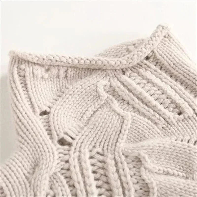 Overhead view of a folded light beige/cream women's high neck/turtleneck jumper. The knit features an elaborate, open-work lace and cable pattern. The garment has a soft, thick appearance and the funnel neck is clearly visible. Focus on the intricate, highly textured stitch work.