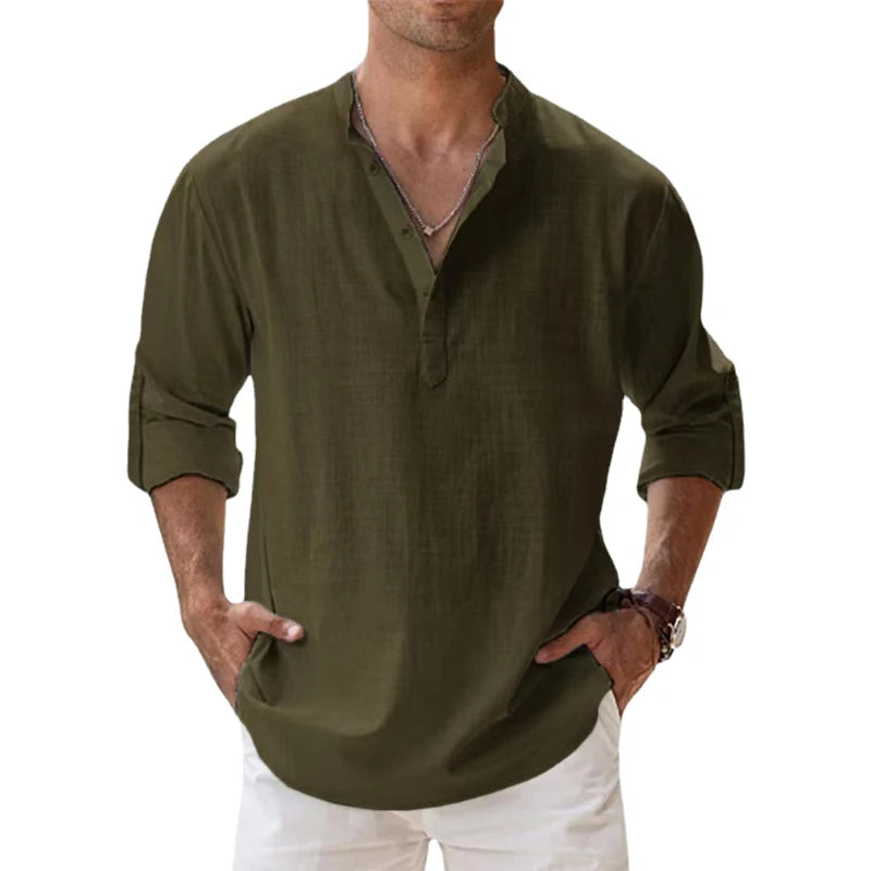 Men's long-sleeve popover shirt in white, featuring a Grandad/band collar and a short buttoned Henley placket. The shirt is made from a light, textured linen-blend fabric. The model is standing with hands in pockets, showcasing the relaxed, slightly oversized fit and rolled-up sleeves. Focus on the texture and the minimalist collar.