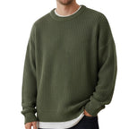 Close-up of a women's cropped, button-front sleeveless vest in a pale yellow/beige colour. The vest features a dense, chunky cable knit pattern and large brown round buttons. It is styled layered over a long-sleeve white shirt and tucked into light blue denim jeans. Focus on the rich cable texture and the cropped length.