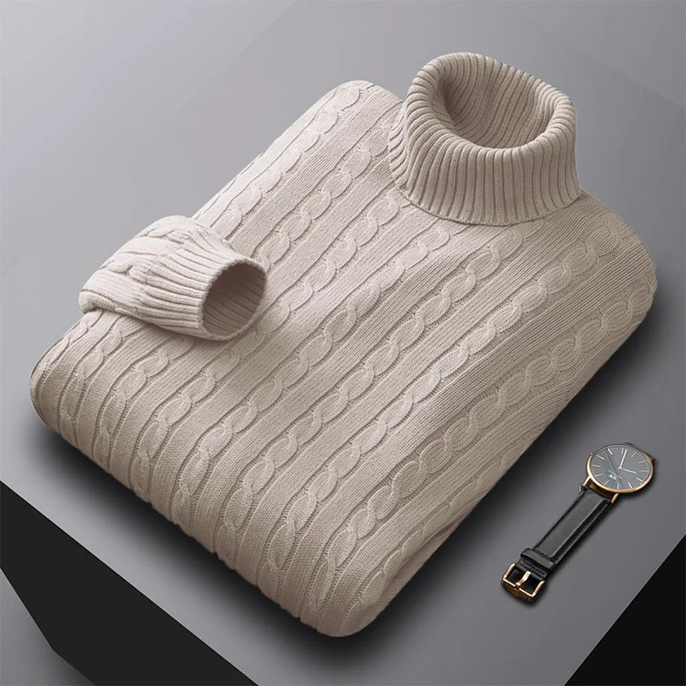Folded men's turtleneck/roll-neck jumper in a light beige/oatmeal colour. The knit features a subtle vertical cable pattern down the body. The turtleneck and cuffs are ribbed. The sweater is styled next to a black leather men's wristwatch. Focus on the fine cable texture and the clean fold.