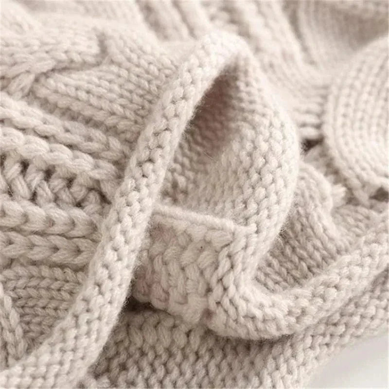 Overhead view of a folded light beige/cream women's high neck/turtleneck jumper. The knit features an elaborate, open-work lace and cable pattern. The garment has a soft, thick appearance and the funnel neck is clearly visible. Focus on the intricate, highly textured stitch work.