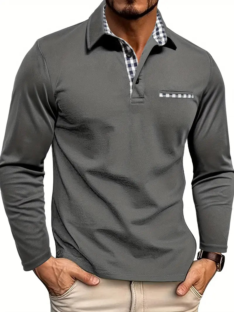 Men's long-sleeve polo shirt in a dark grey/charcoal stretch fabric with a three-button placket. The shirt features an open collar lined with blue and white gingham check fabric, and a matching gingham trim detail on the mock chest pocket. The model is standing with hands in light beige trousers pockets, showcasing the tailored fit. Focus on the contrast collar detail and the smooth texture of the fabric.